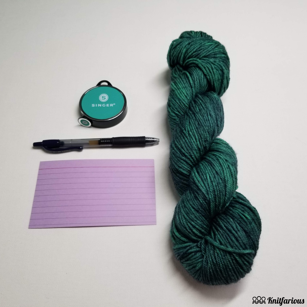 hand dyed yarn hank in dk weight, retractable measuring tape, colored index card, and retractable Pilot G-2 pen. 