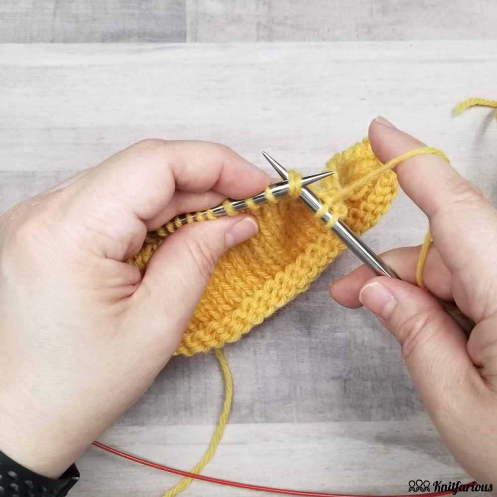 yellow wool swatch showing how to insert your right needle into the next two stitches on your left hand needle through the back loops to k2tog tbl